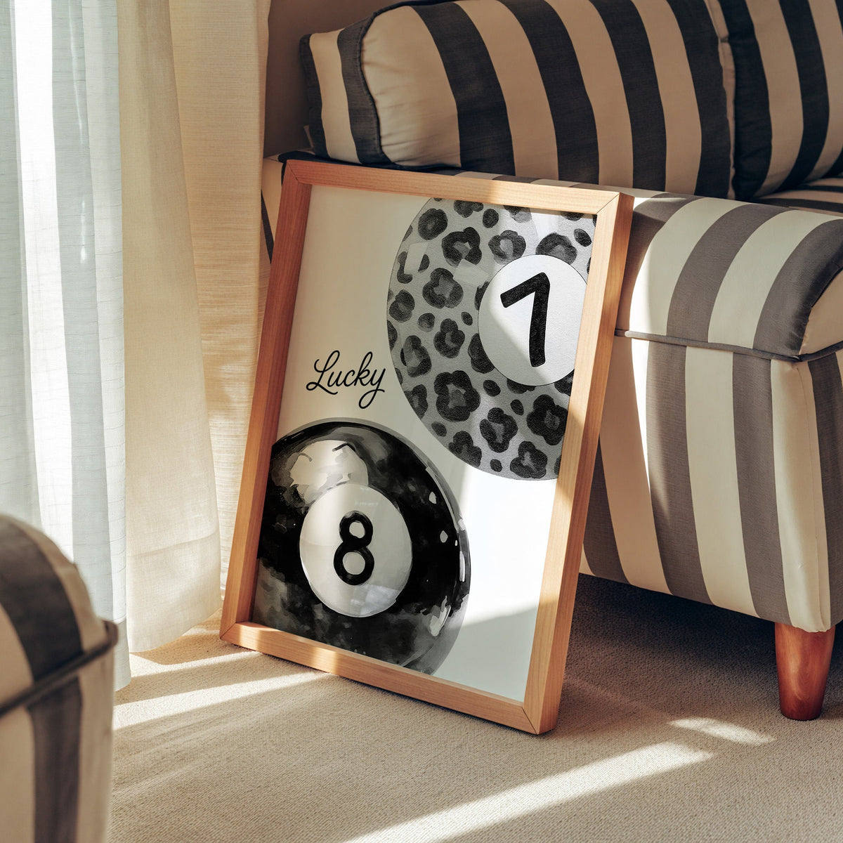 Leopard seven ball and black eight ball watercolor print in a pine frame leaning against a striped armchair