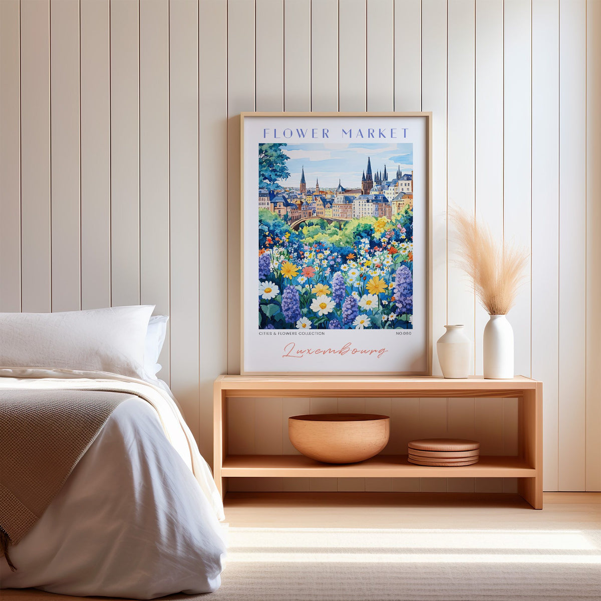 Luxembourg flower market print in an oak frame on a wood bench against a white shiplap bedroom wall with pampas grass