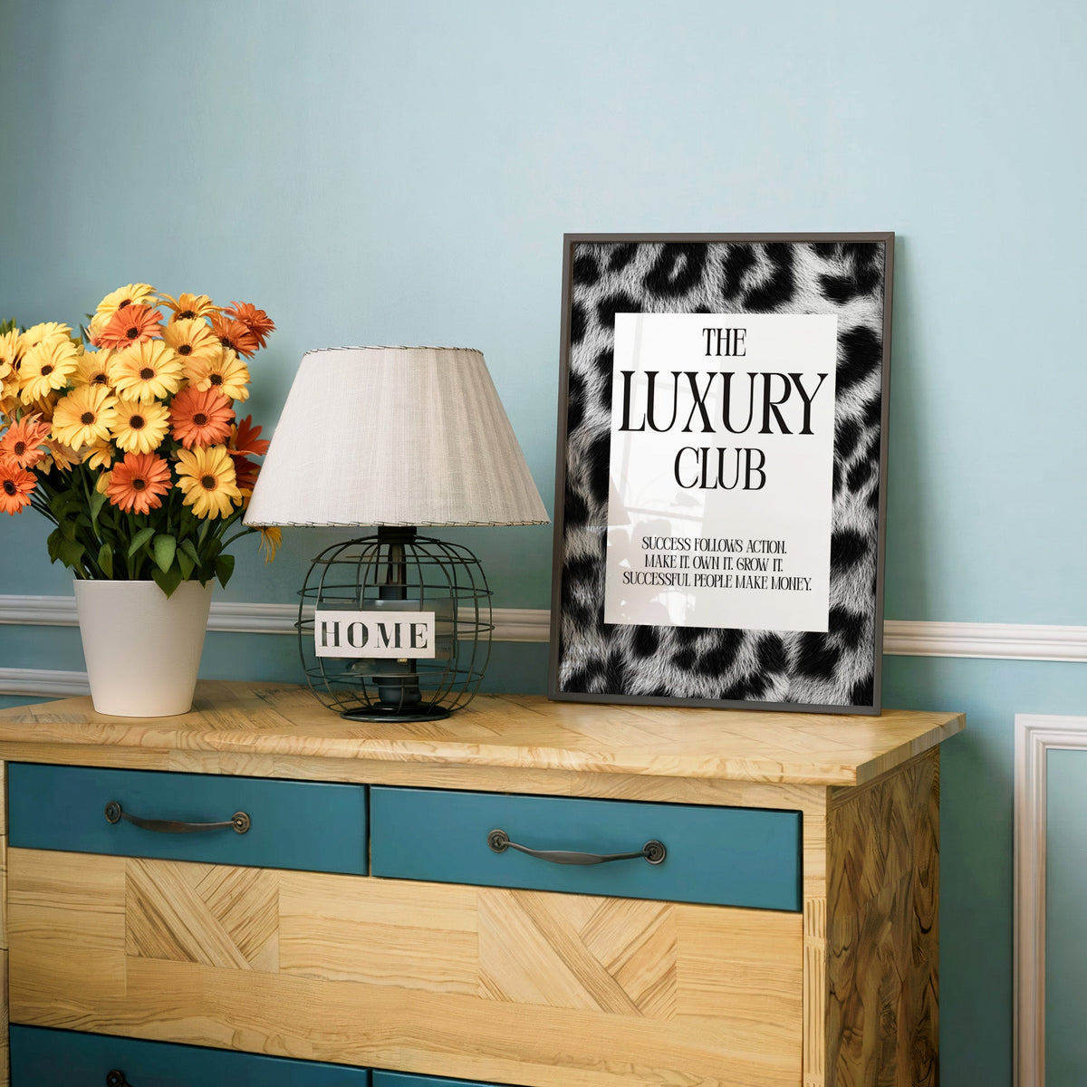 Luxury club serif typography on leopard fur print in a charcoal frame on a teal dresser beside orange daisies