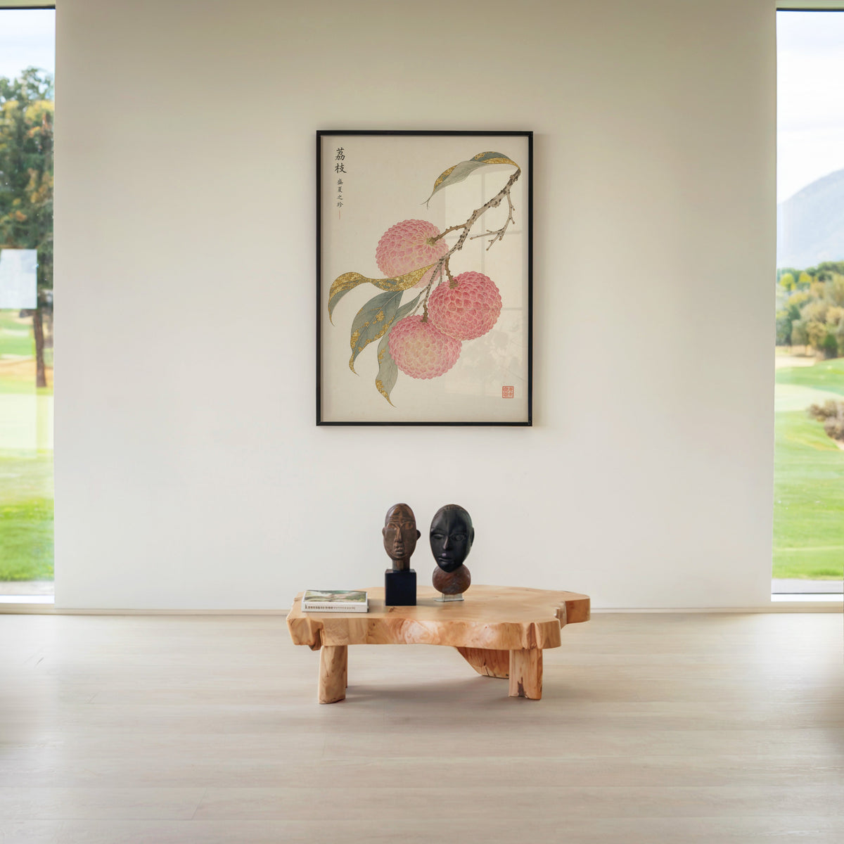 lychee branch with gold-toned leaves print in a black frame above a live-edge wood coffee table between garden windows