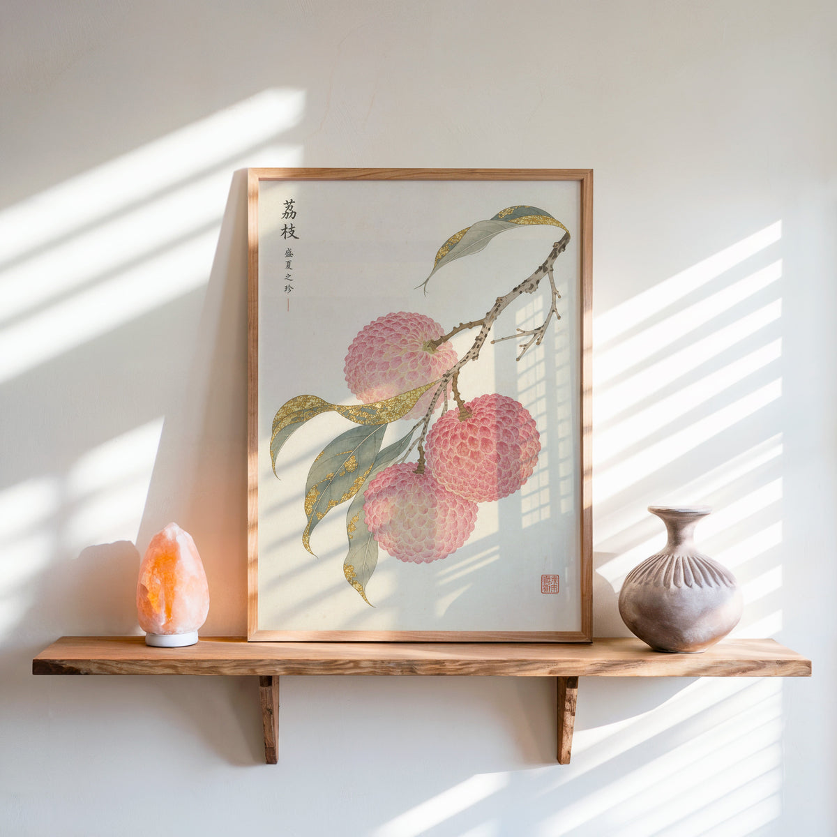 lychee branch with gold-toned leaves print in an oak frame on a live-edge wall shelf with a salt lamp and clay vase