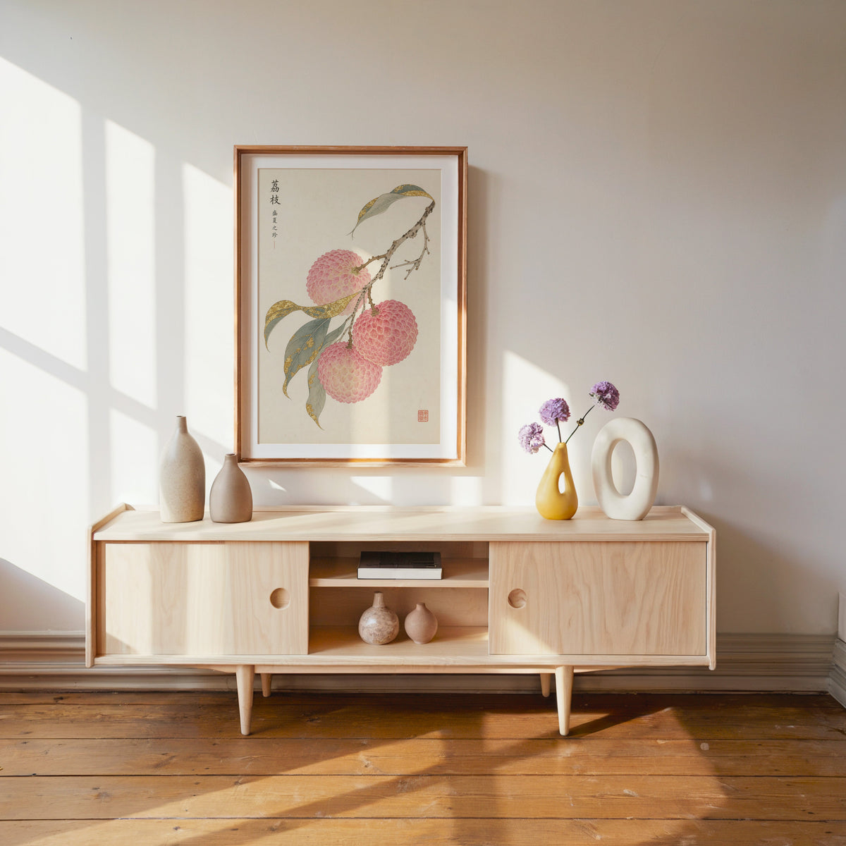 lychee branch with gold-toned leaves print shown in a wood frame with a white mat above a pale wood media console