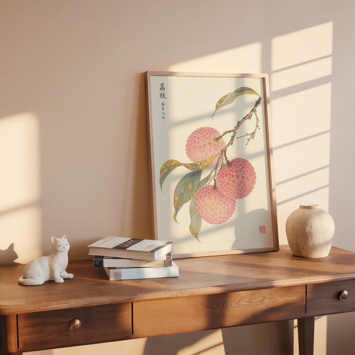 lychee branch with gold-toned leaves print shown in a rose gold frame leaning on a wooden writing desk with books