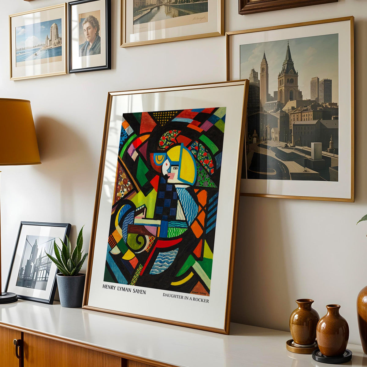Modern art print shown in a gold frame leaning on a sideboard in a gallery wall