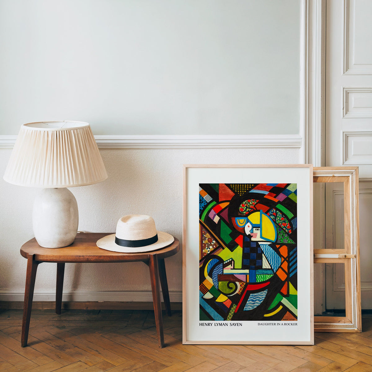 Sayen poster in a light wood frame leaning by a bench and panama hat