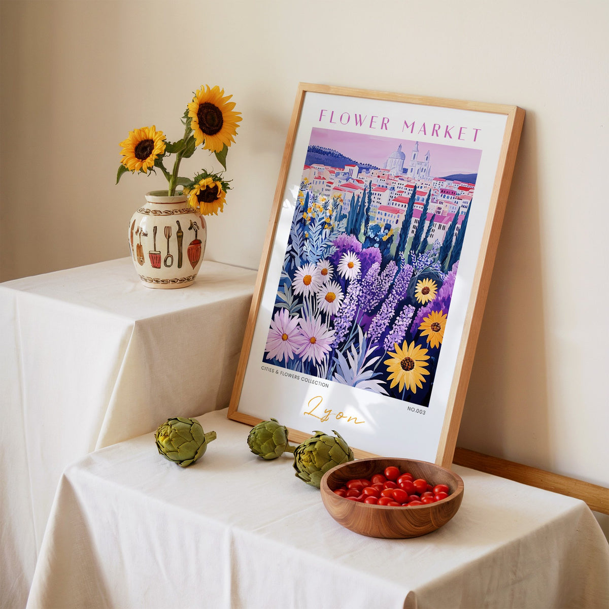 Lyon flower market print in an oak frame leaning on a linen-draped table beside a vase of sunflowers