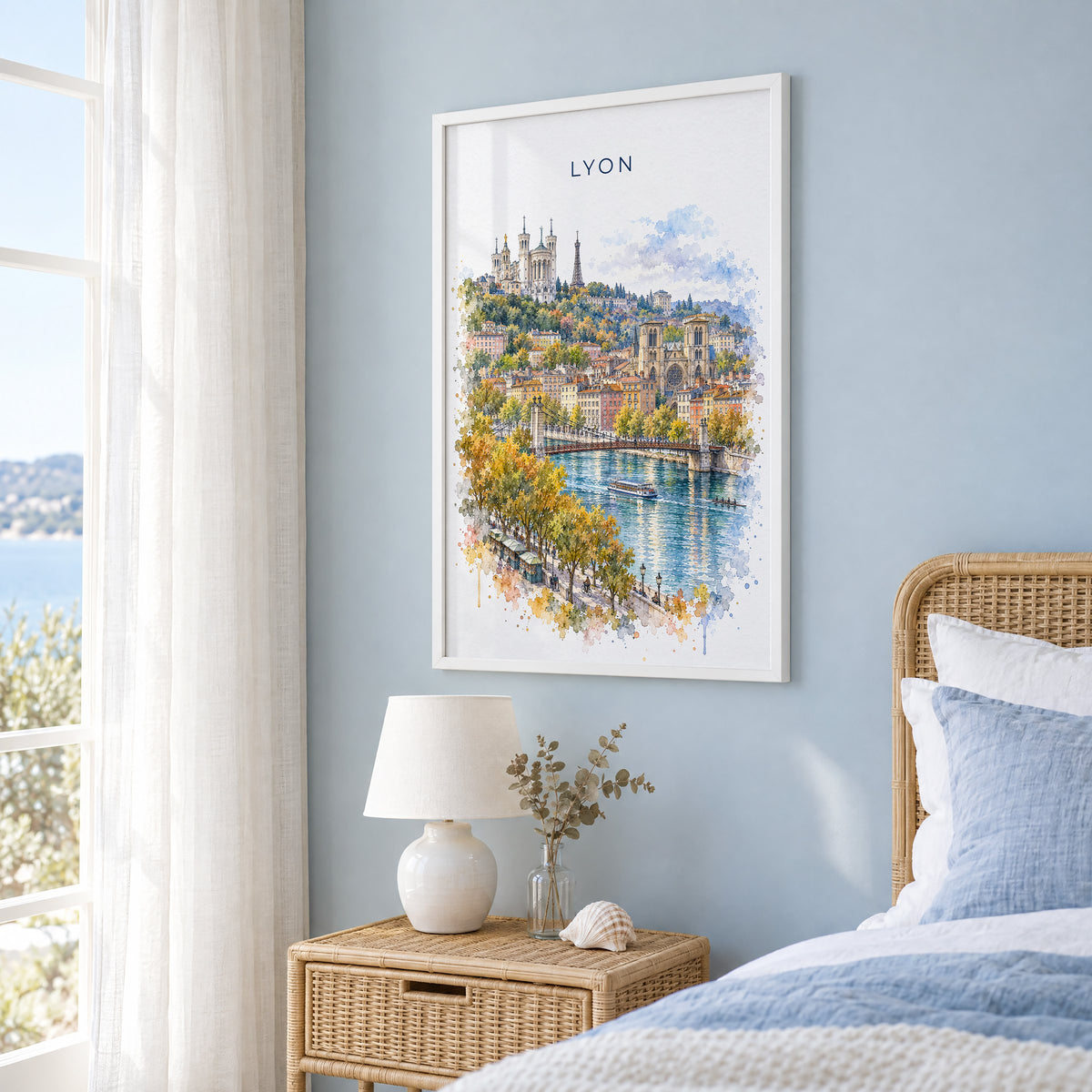 Lyon watercolor print in a white frame on a pale blue wall beside a rattan bed in a coastal bedroom