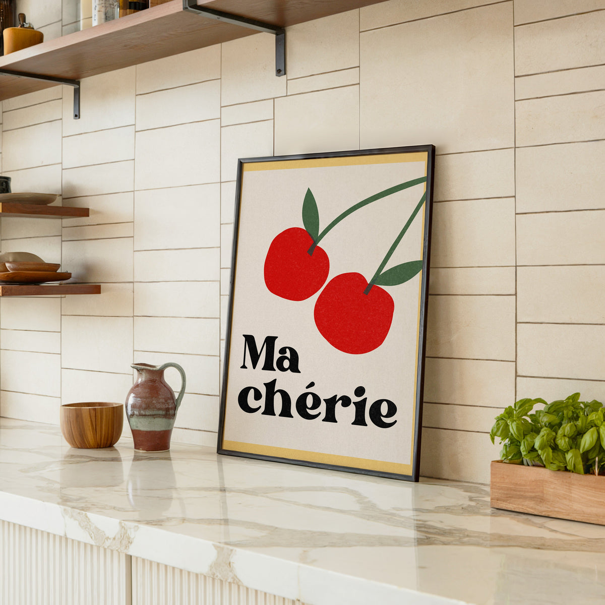 Ma Cherie cherries print in a black frame leaning on a marble counter in a tiled kitchen