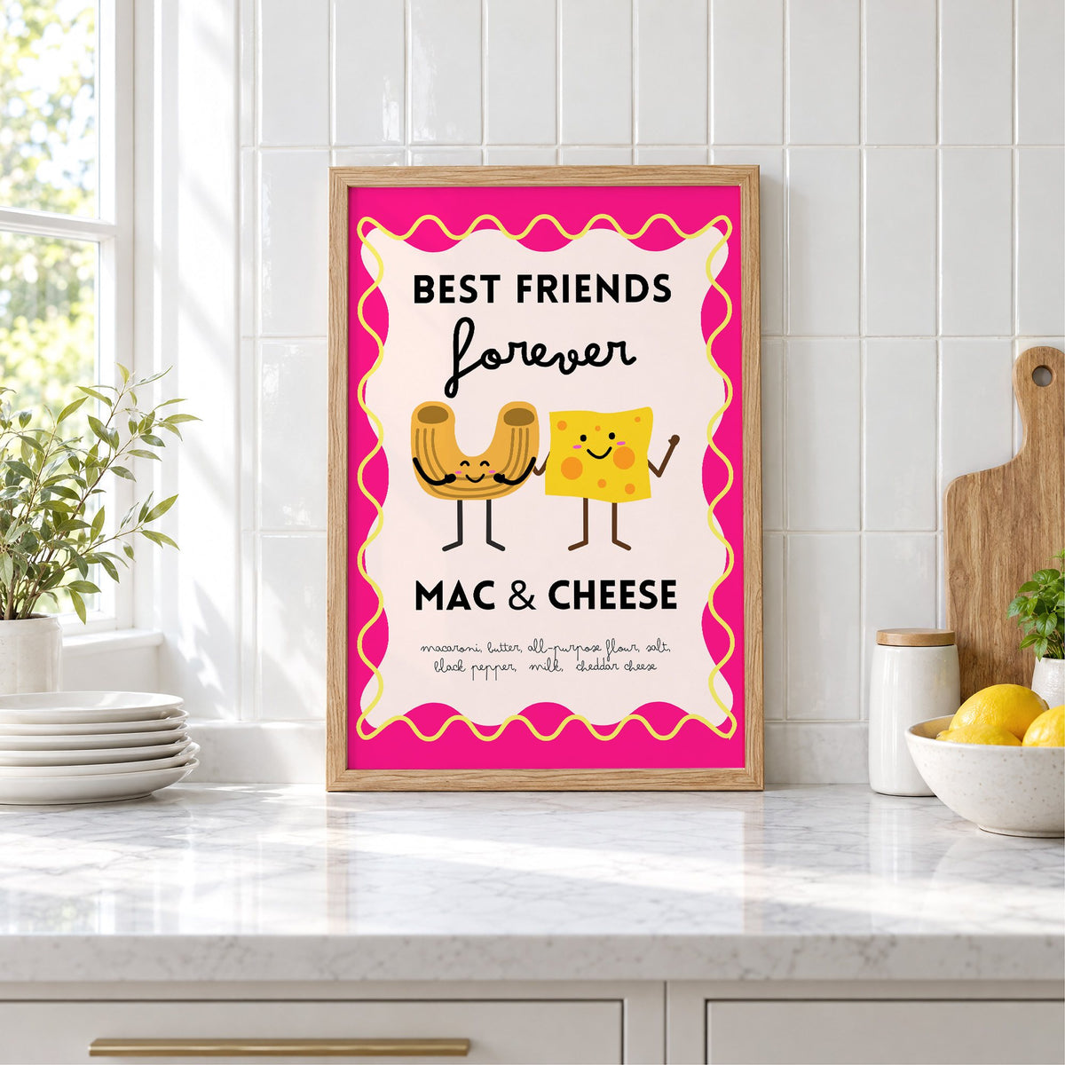 Mac and cheese best friends pink print in an oak frame leaning on a marble counter by white tiles and lemons