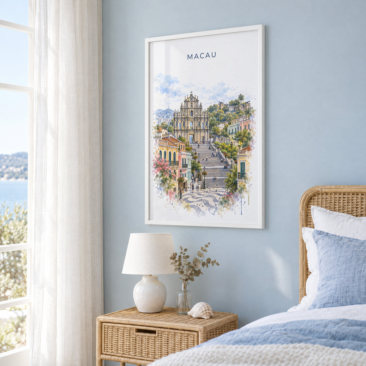 Macau watercolor print in a white frame on a pale blue wall beside a rattan bed in a coastal bedroom