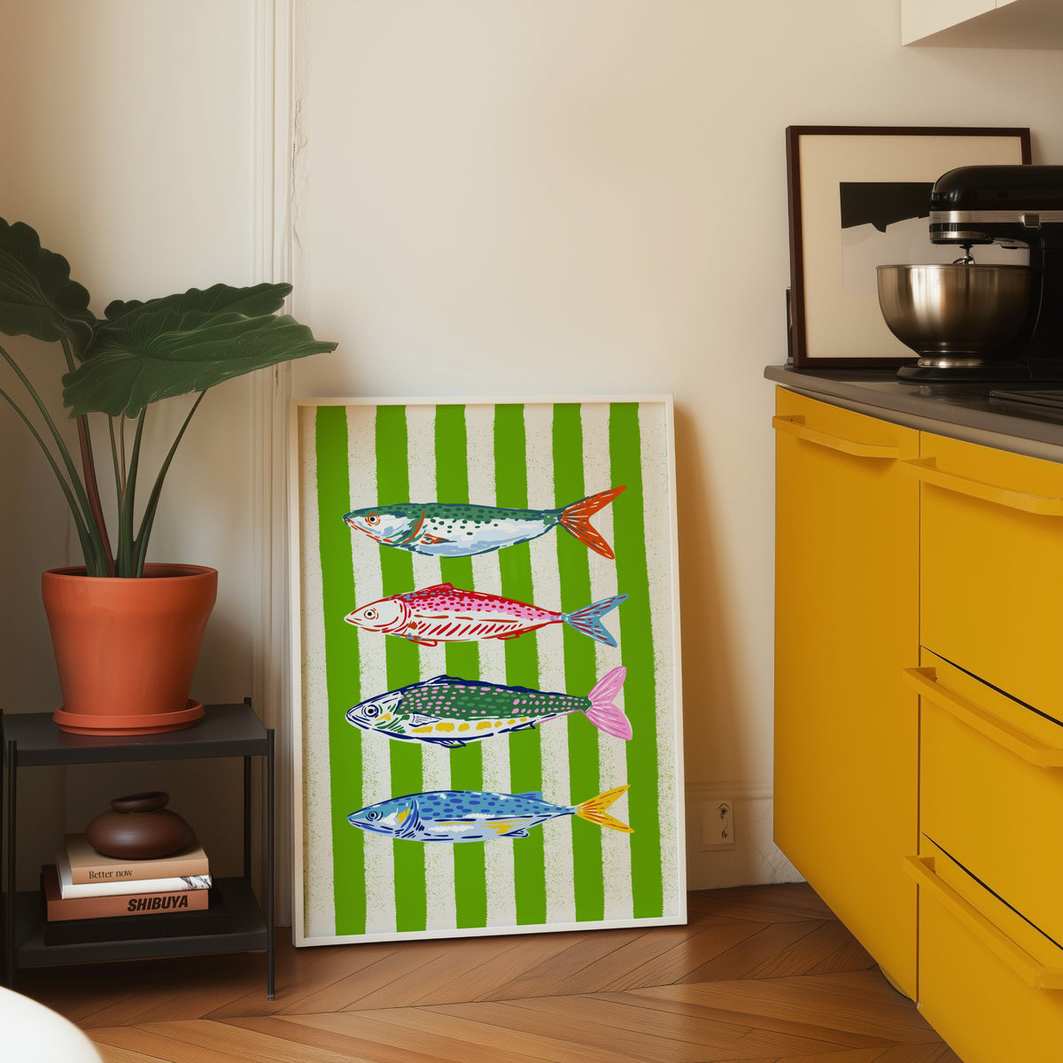 Mackerel row print in a white frame leaning on parquet beside a bright yellow kitchen