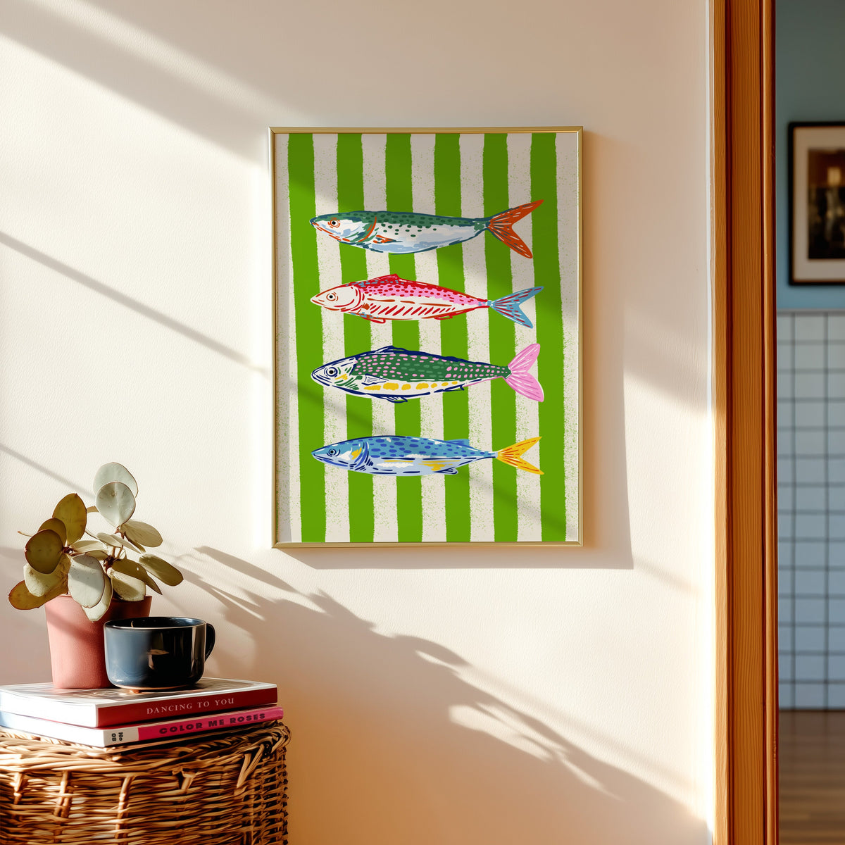 Mackerel row print shown in a gold frame above a basket of books and a pilea plant