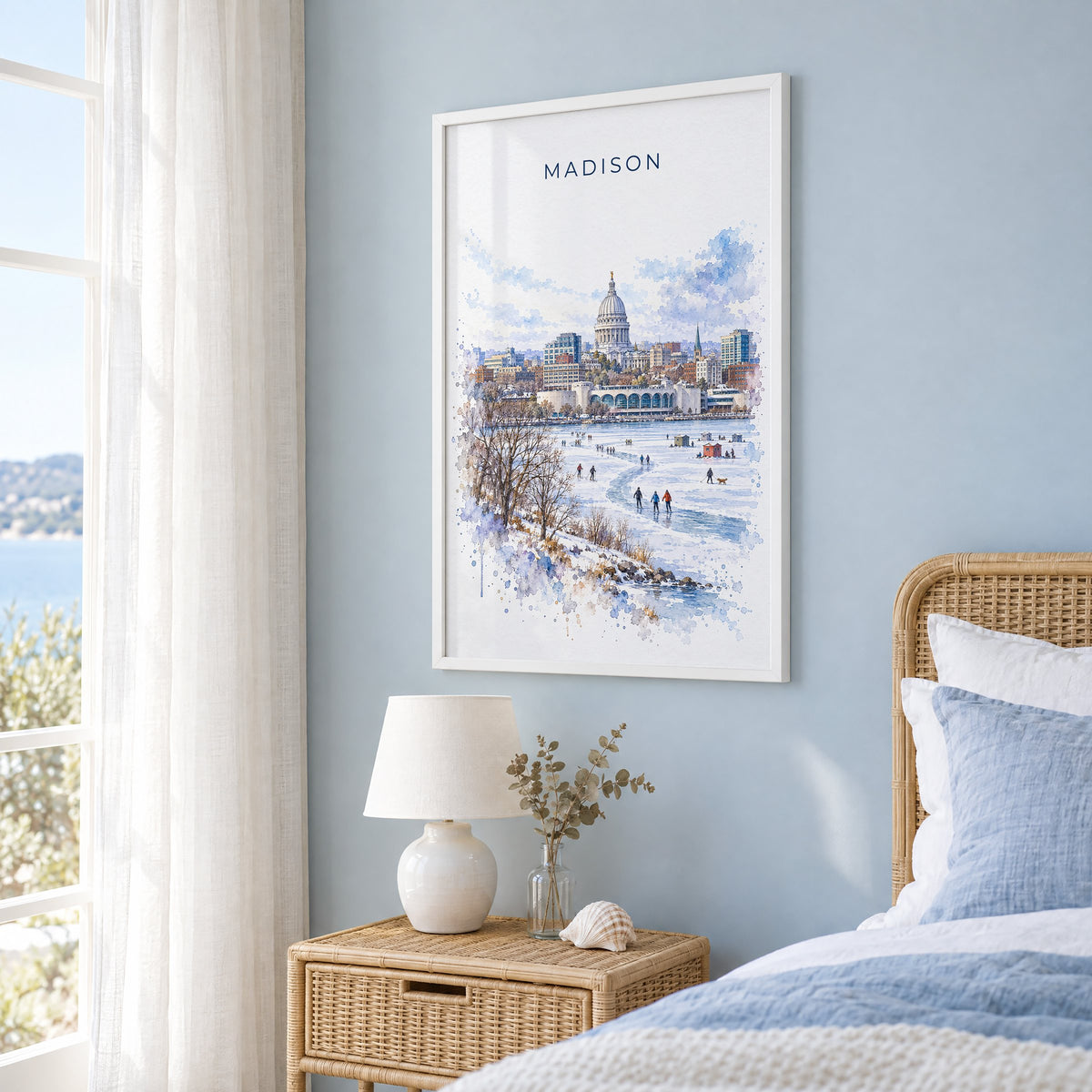 Madison watercolor print in a white frame on a pale blue wall beside a rattan bed in a coastal bedroom