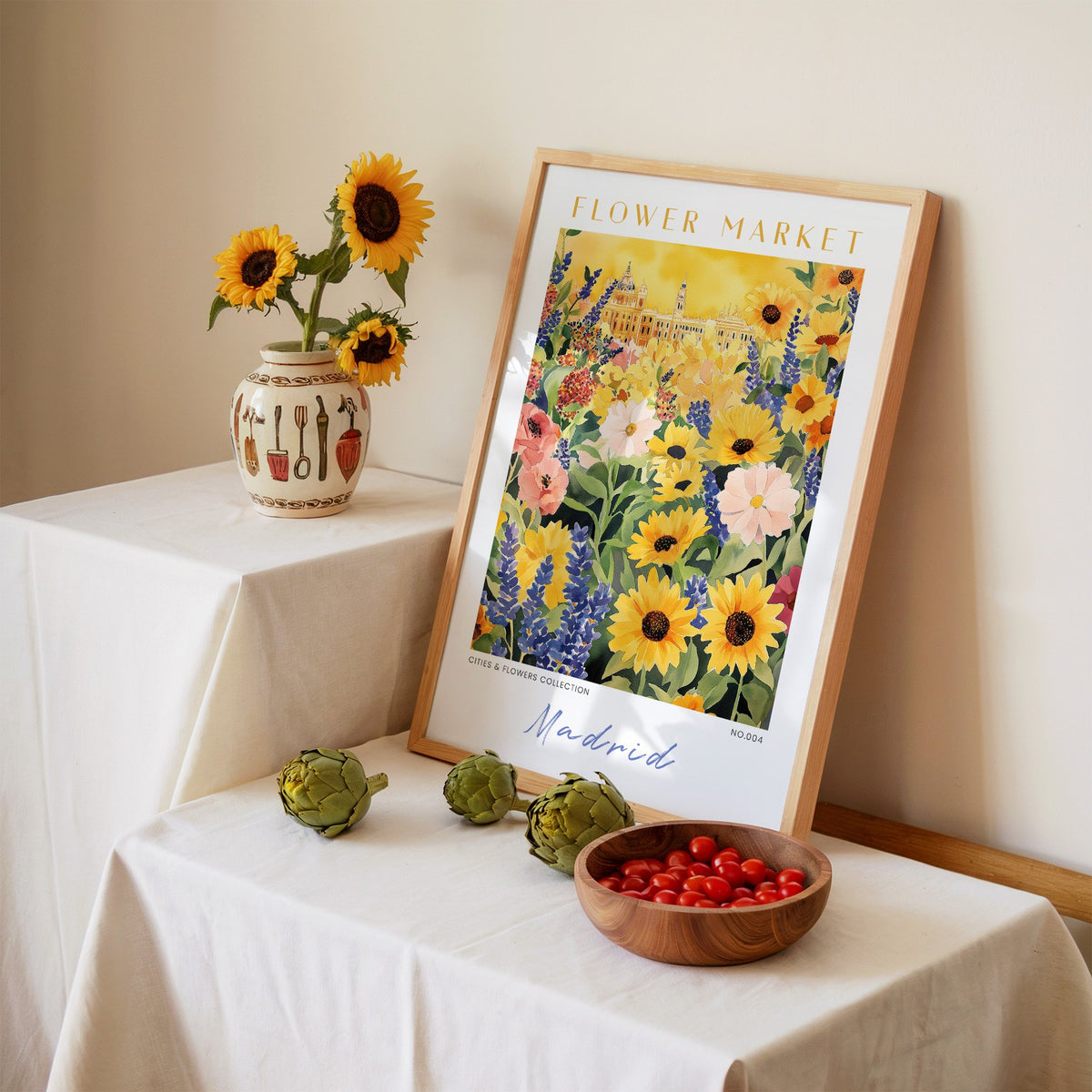 Madrid flower market print in an oak frame leaning on a linen-draped table beside a vase of sunflowers