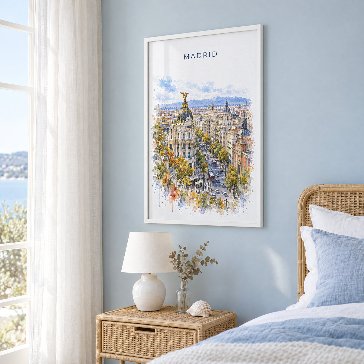 Madrid watercolor print in a white frame on a pale blue wall beside a rattan bed in a coastal bedroom