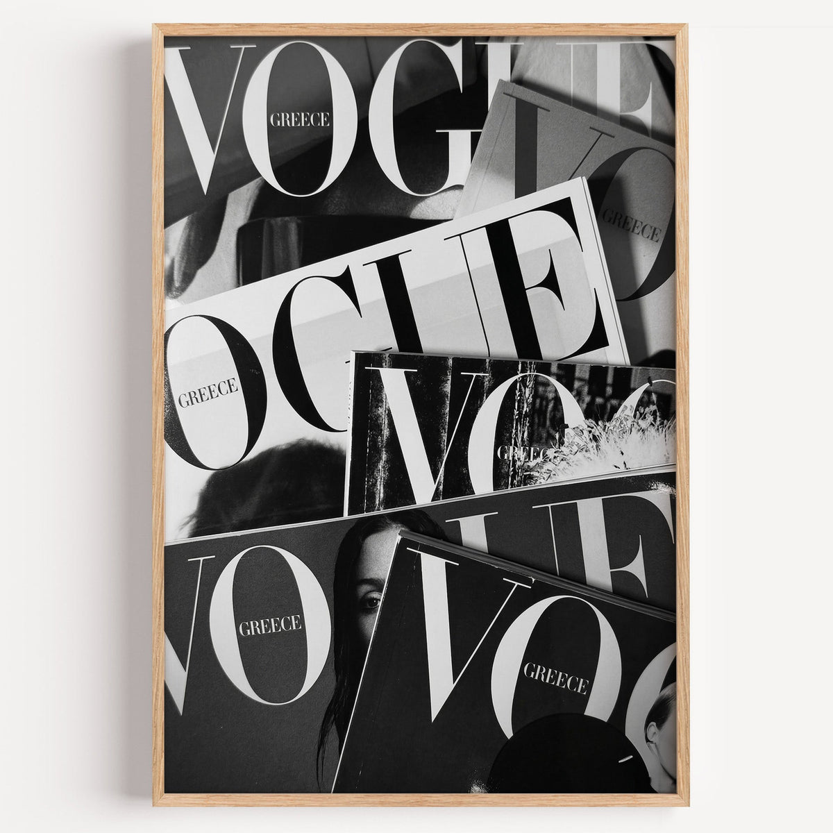 Overlapping magazine covers with giant lettering print in a light oak frame on a plain white wall