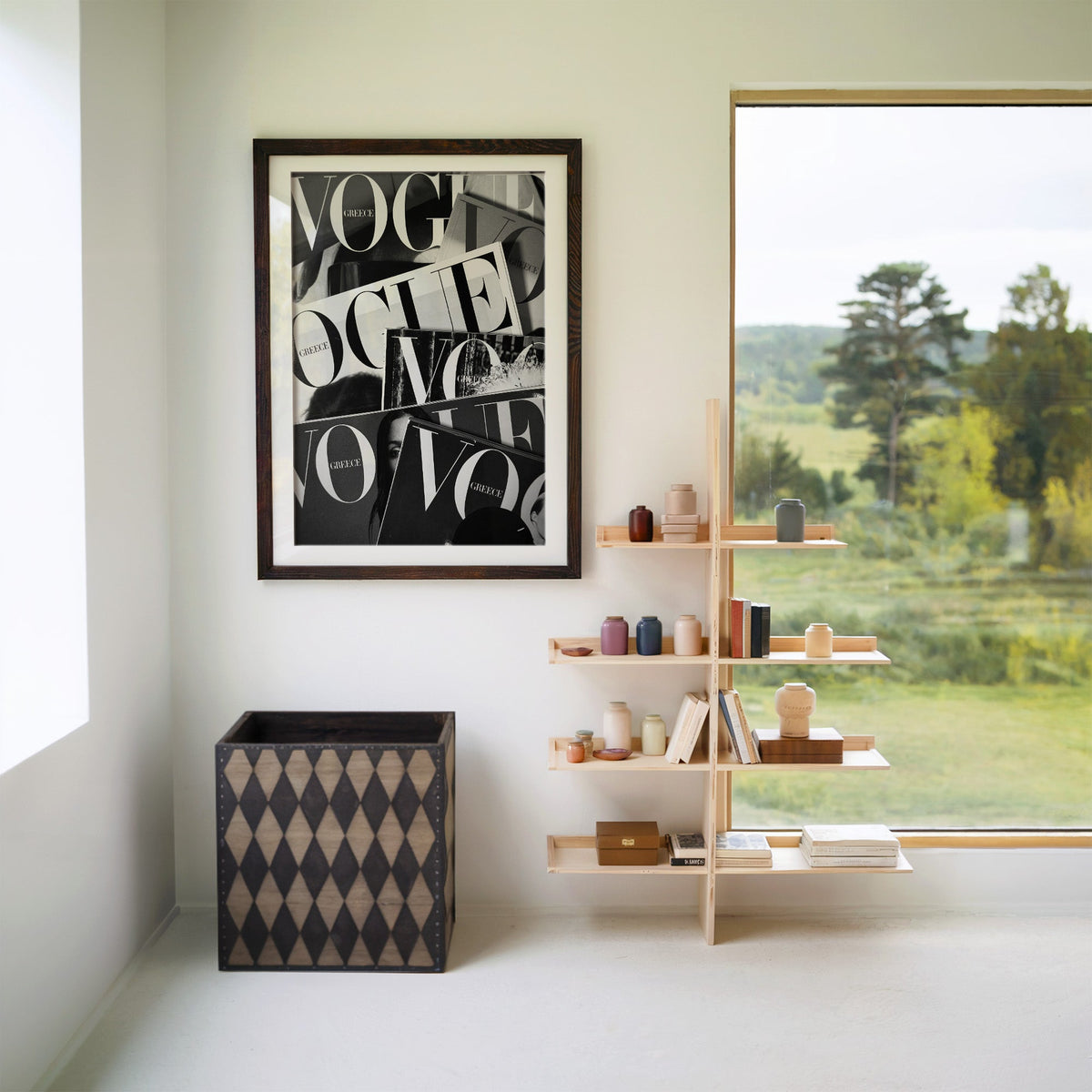 Overlapping magazine covers with giant lettering print in a walnut frame with a white mat beside wooden shelves and a garden window