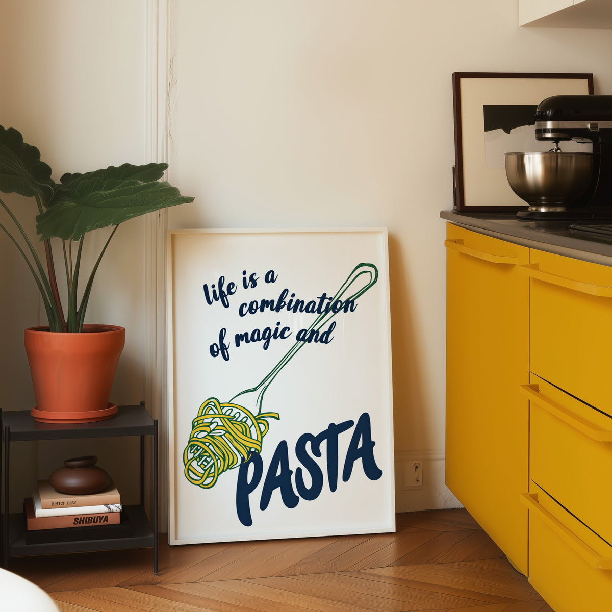 Magic and Pasta print in a white frame leaning on parquet beside a bright yellow kitchen