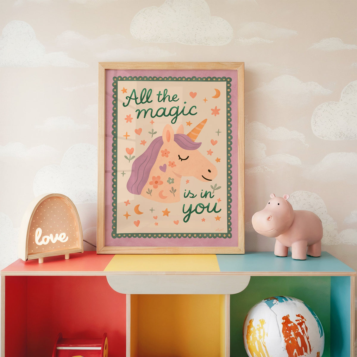 Magic is in you unicorn nursery print in an oak frame on a rainbow toy shelf against cloud wallpaper