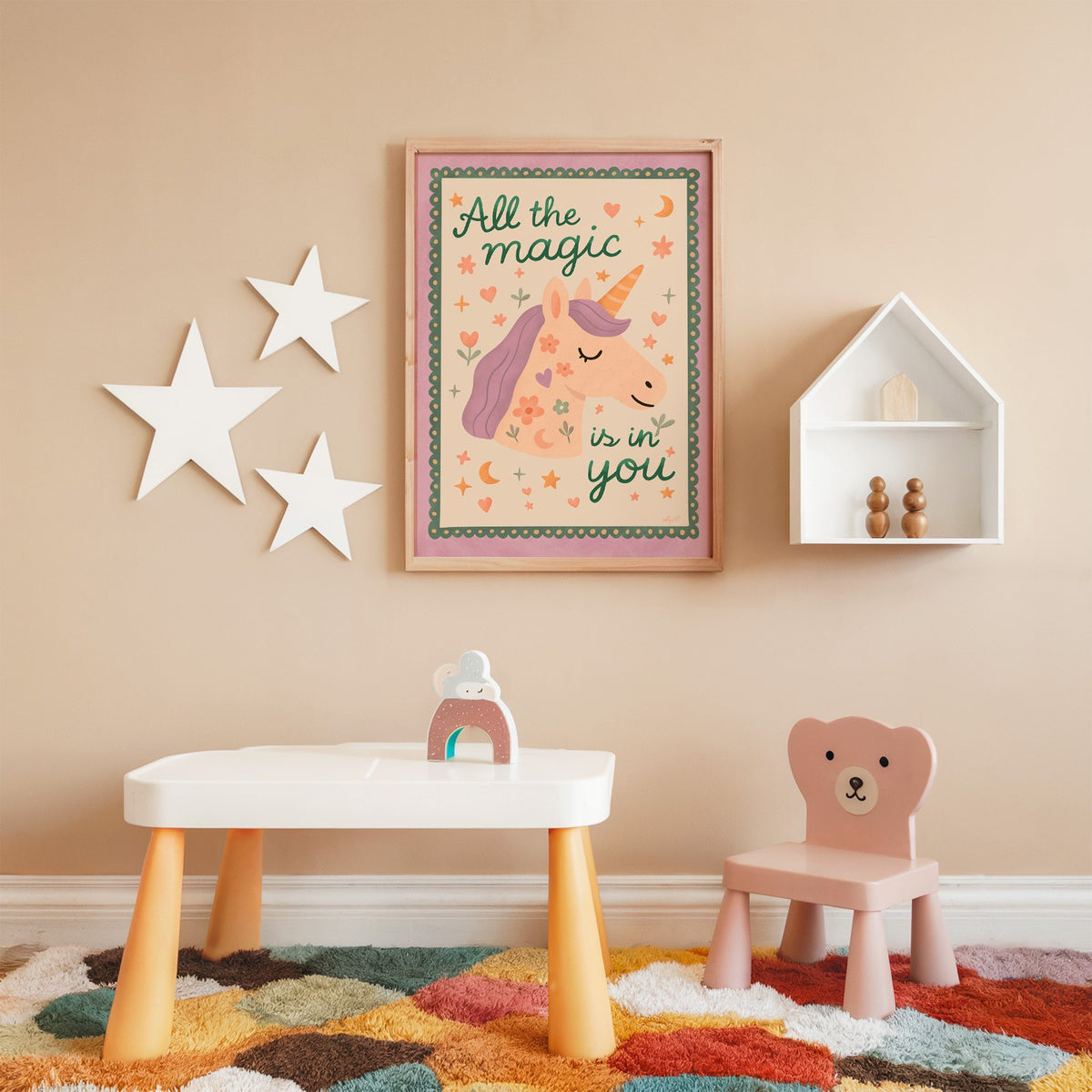 Magic is in you unicorn nursery print in an oak frame on a peach wall above a kids table with wall stars