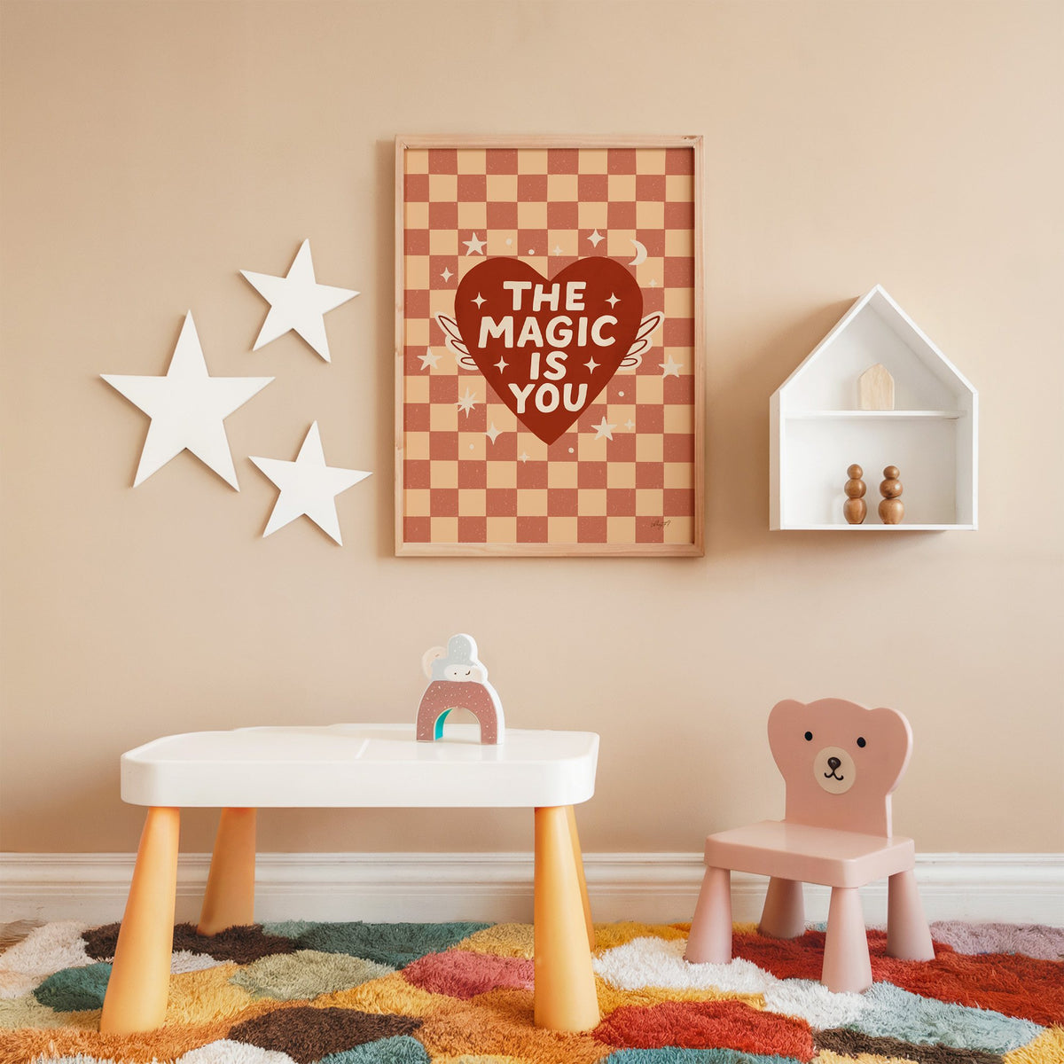 The magic is you winged heart nursery print in an oak frame on a peach wall above a kids table with wall stars