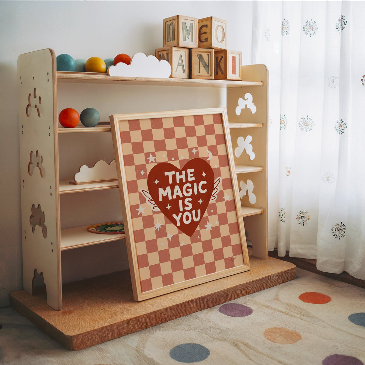 The magic is you winged heart nursery print in an oak frame leaning on a toy shelf with wooden letter blocks