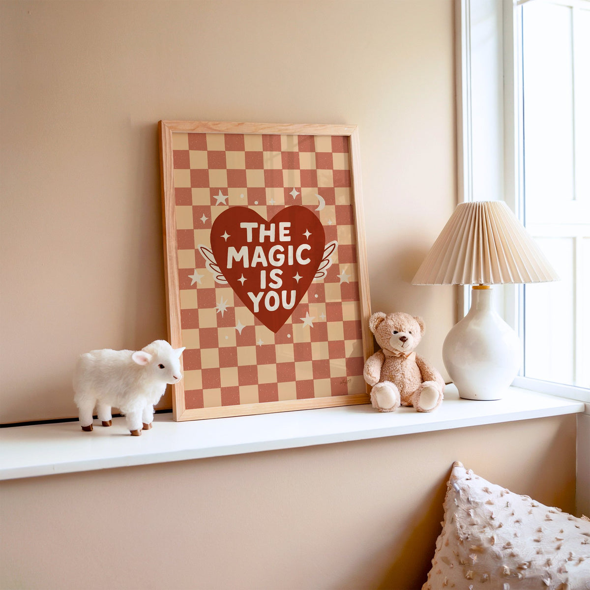 The magic is you winged heart nursery print in an oak frame on a window ledge with a toy lamb and teddy