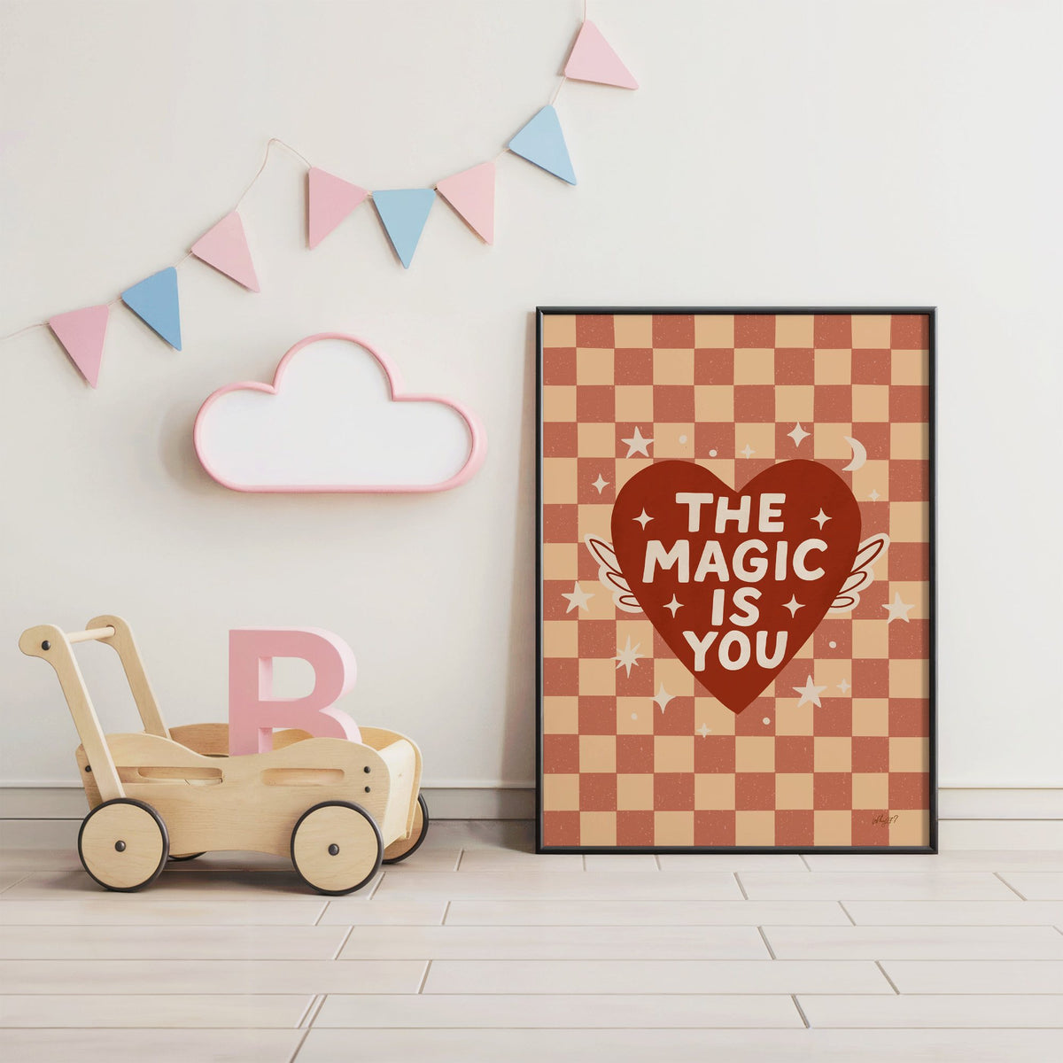 The magic is you winged heart nursery print in a black frame under pastel bunting by a wooden baby walker