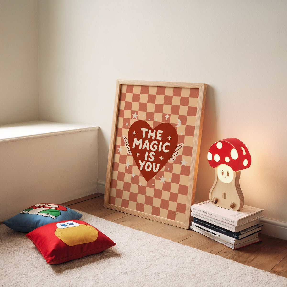 The magic is you winged heart nursery print in an oak frame leaning on a rug beside a mushroom lamp and floor cushions