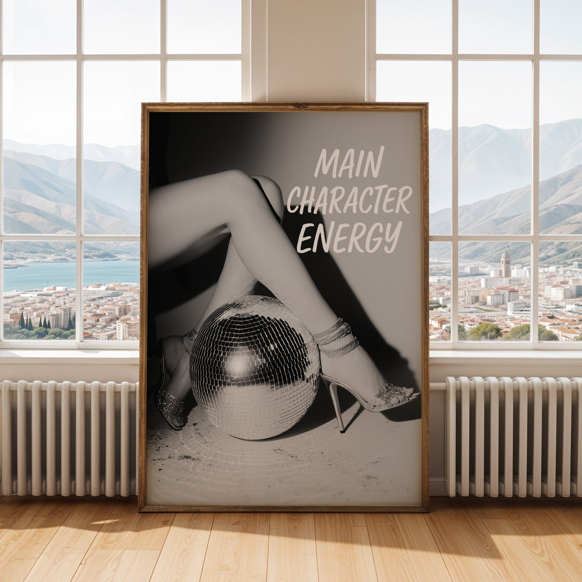 Crossed legs in heels beside disco ball print shown in an antique gold frame by tall windows with a sea view