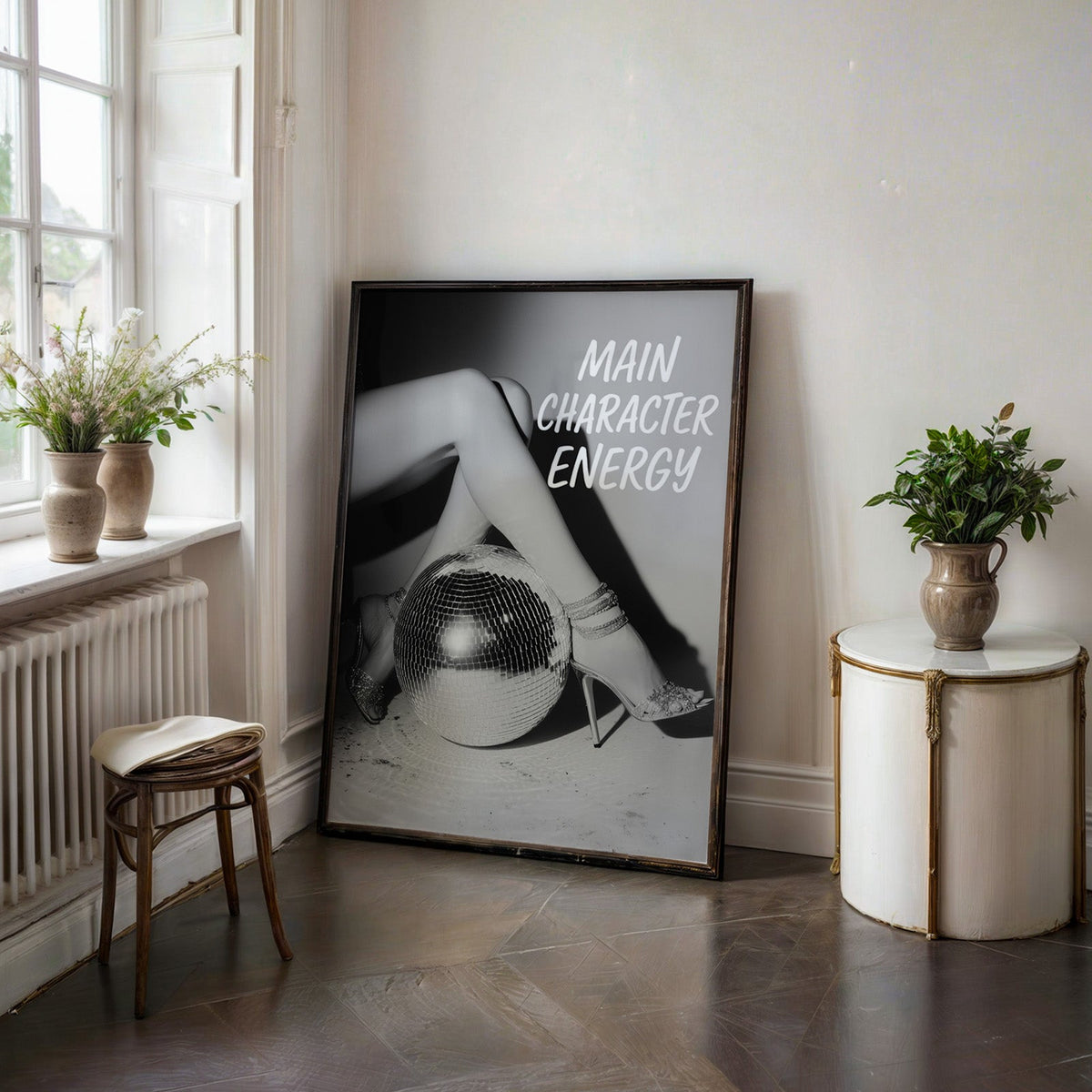 Crossed legs in heels beside disco ball print in a black frame on a dark stone floor beside a white side table