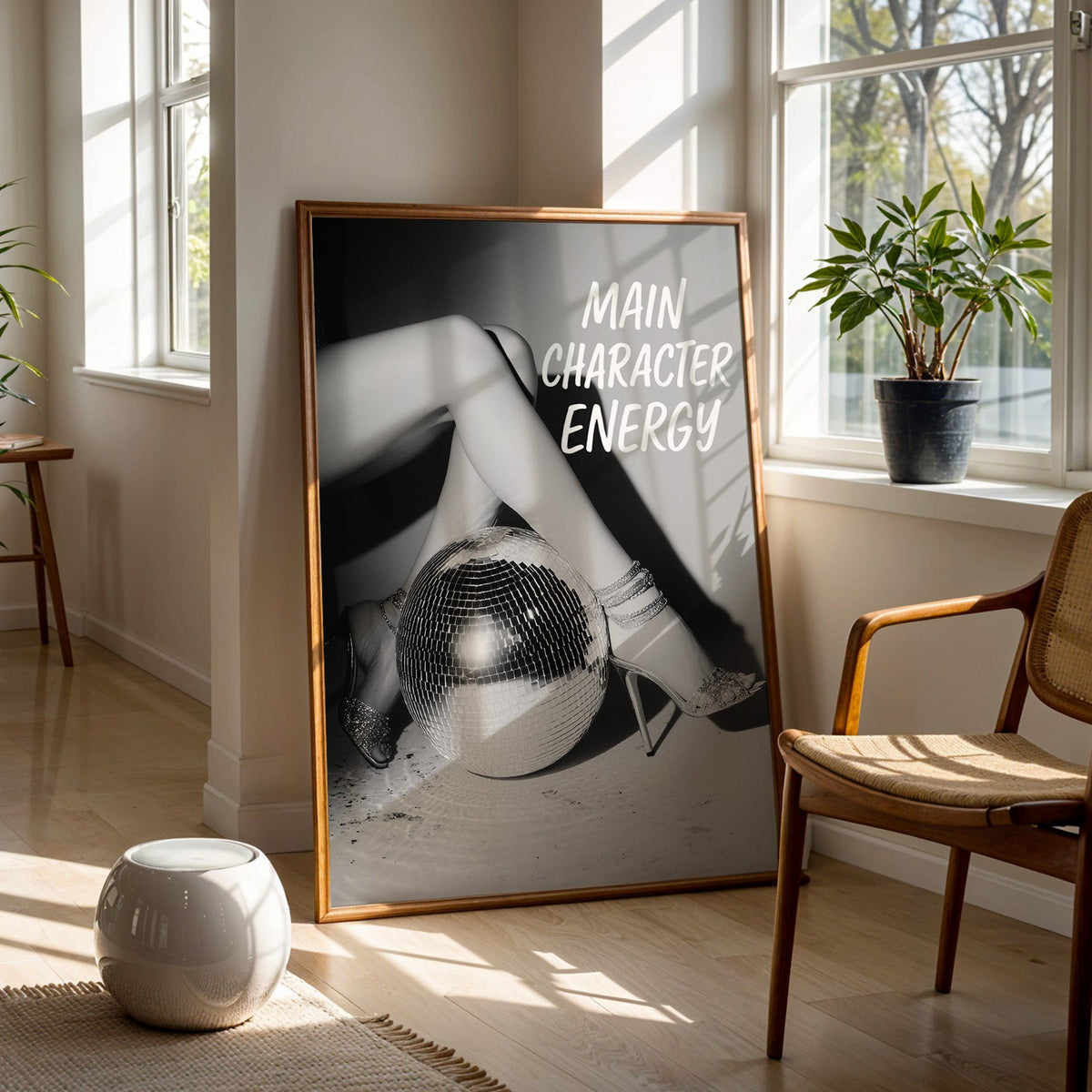 Crossed legs in heels beside disco ball print in a walnut frame on a wood floor beside a cane chair and sunny window