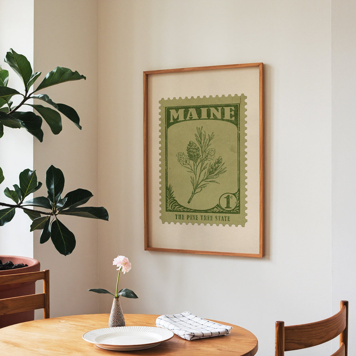 Maine state flower print framed above a round wooden table with a single bloom in a vase and books