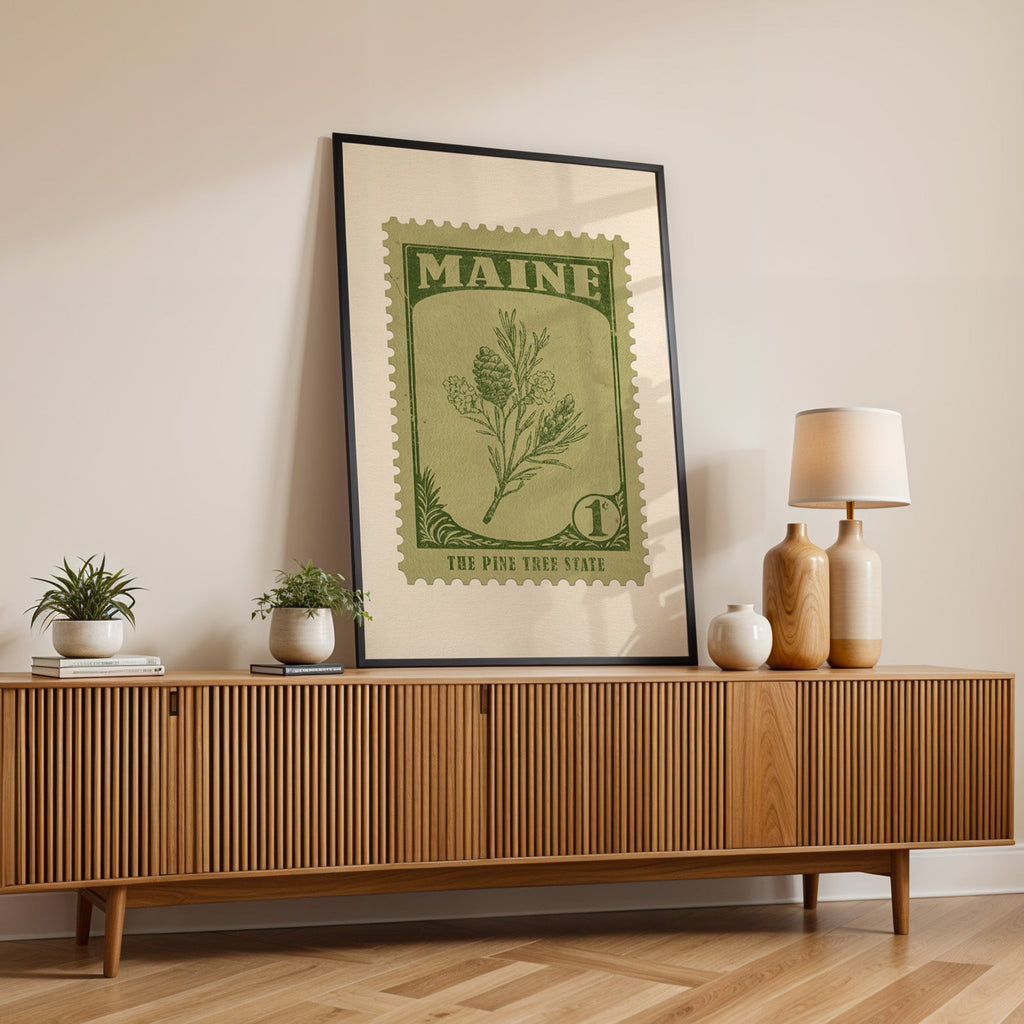 Maine state flower print in a black frame leaning on a fluted wood credenza with vases and a lamp