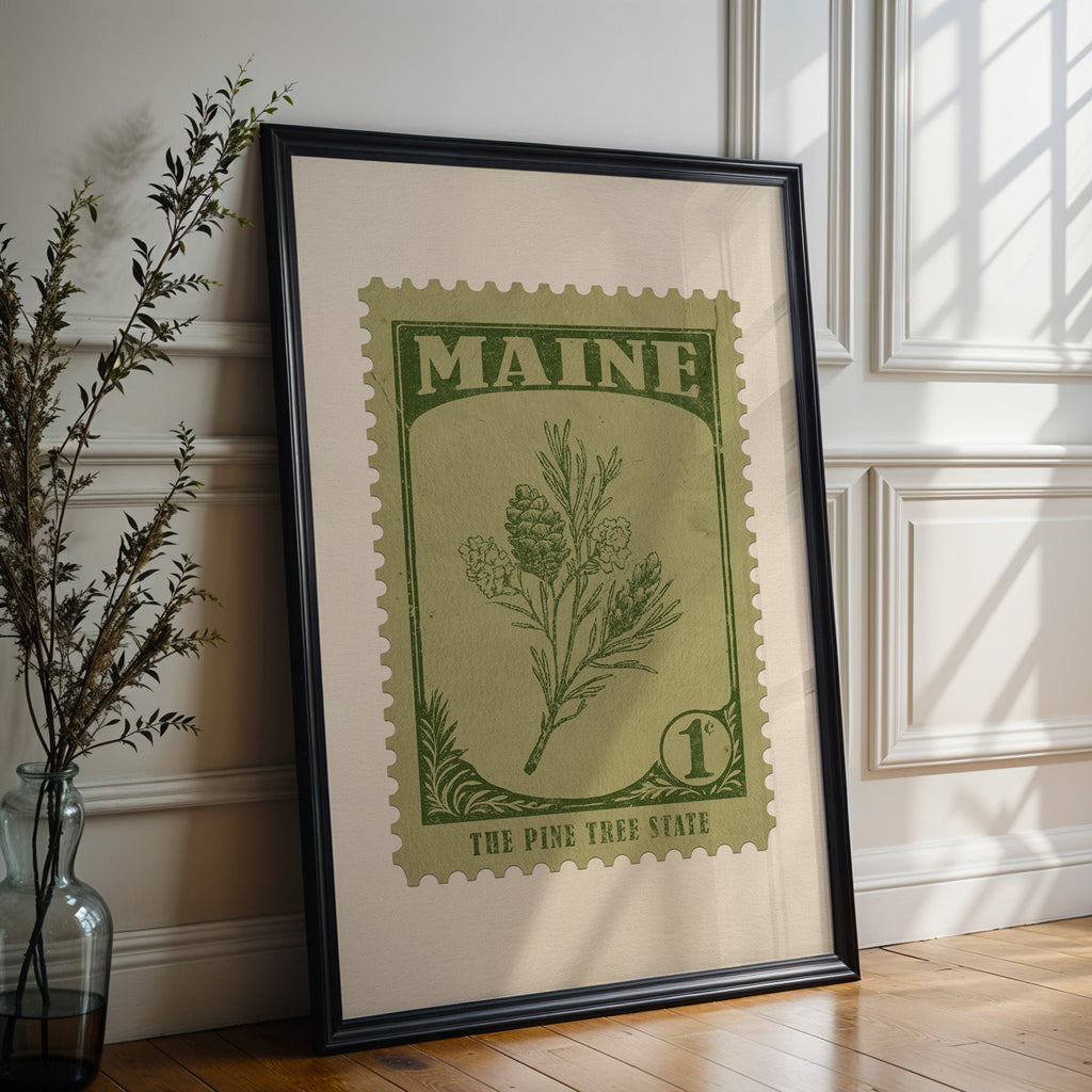 Maine state flower print in a black frame leaning against a white panelled wall beside olive branches