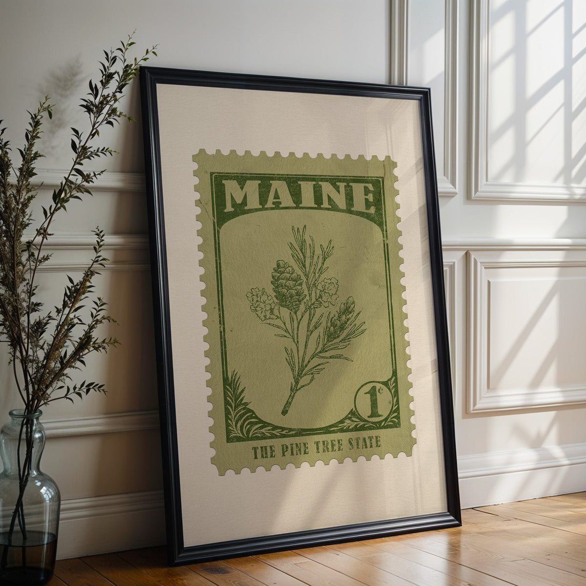 Maine state flower print in a black frame leaning against a white panelled wall beside olive branches