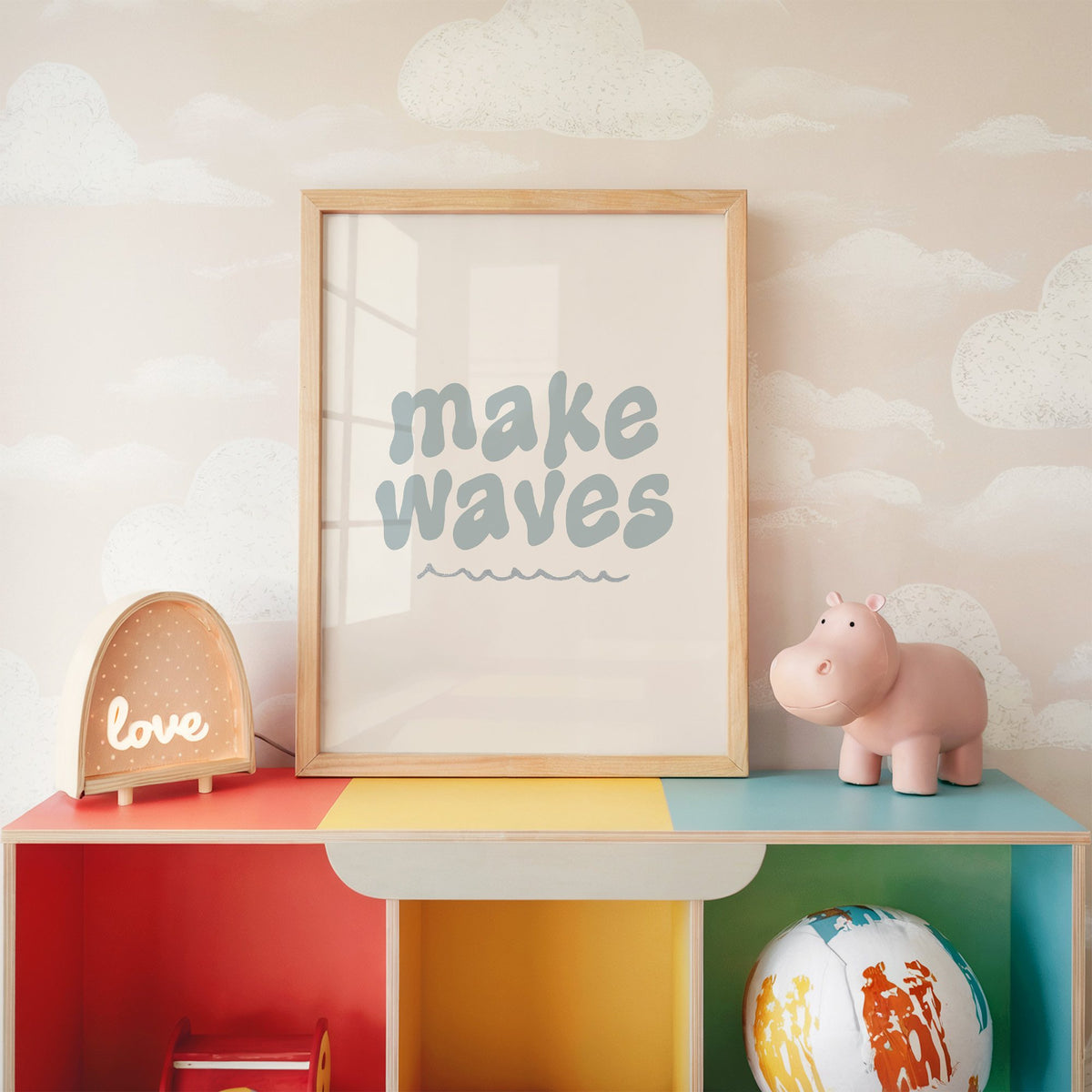 Make waves typography nursery print in an oak frame on a rainbow toy shelf against cloud wallpaper