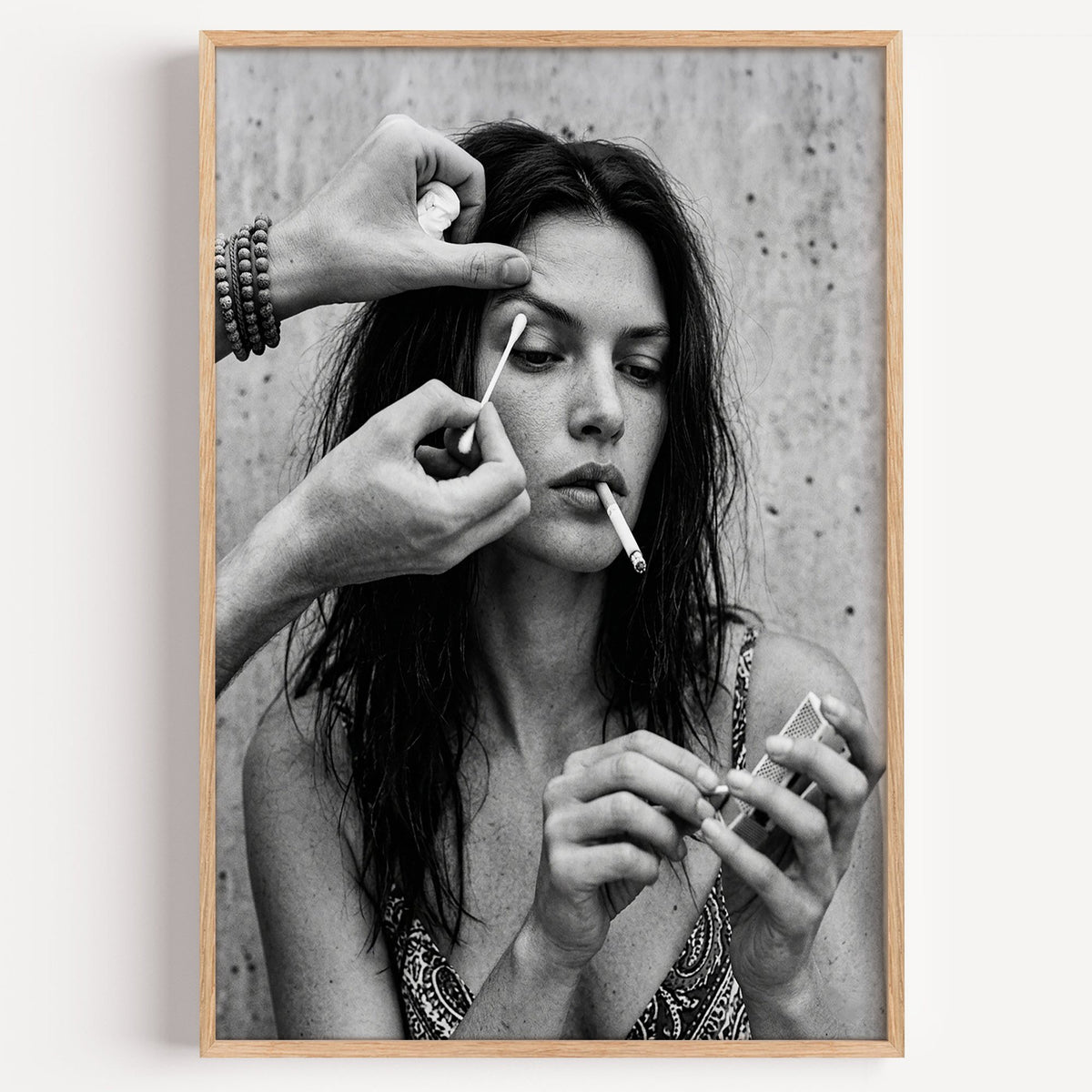 Makeup artist hands with cotton swab at eye print in a light oak frame on a plain white wall