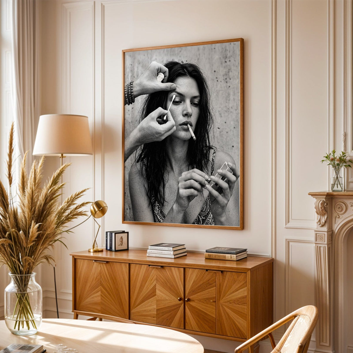 Makeup artist hands with cotton swab at eye print in an oak frame above a sunburst wood sideboard with pampas grass