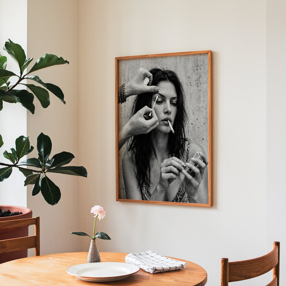 Makeup artist hands with cotton swab at eye print in a teak frame above a round wooden dining table