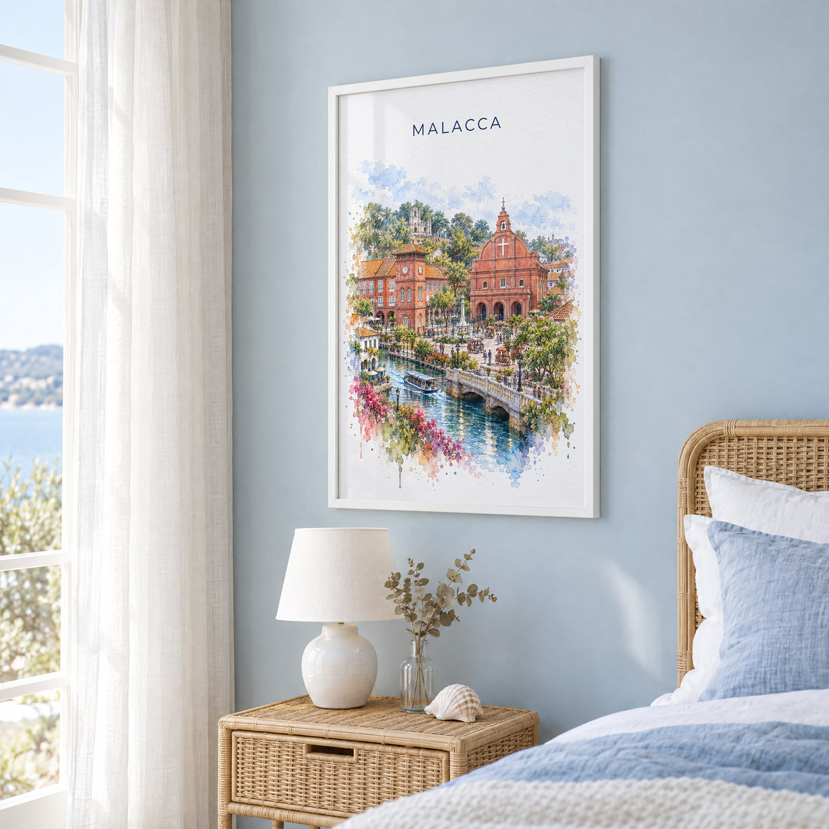 Malacca watercolor print in a white frame on a pale blue wall beside a rattan bed in a coastal bedroom