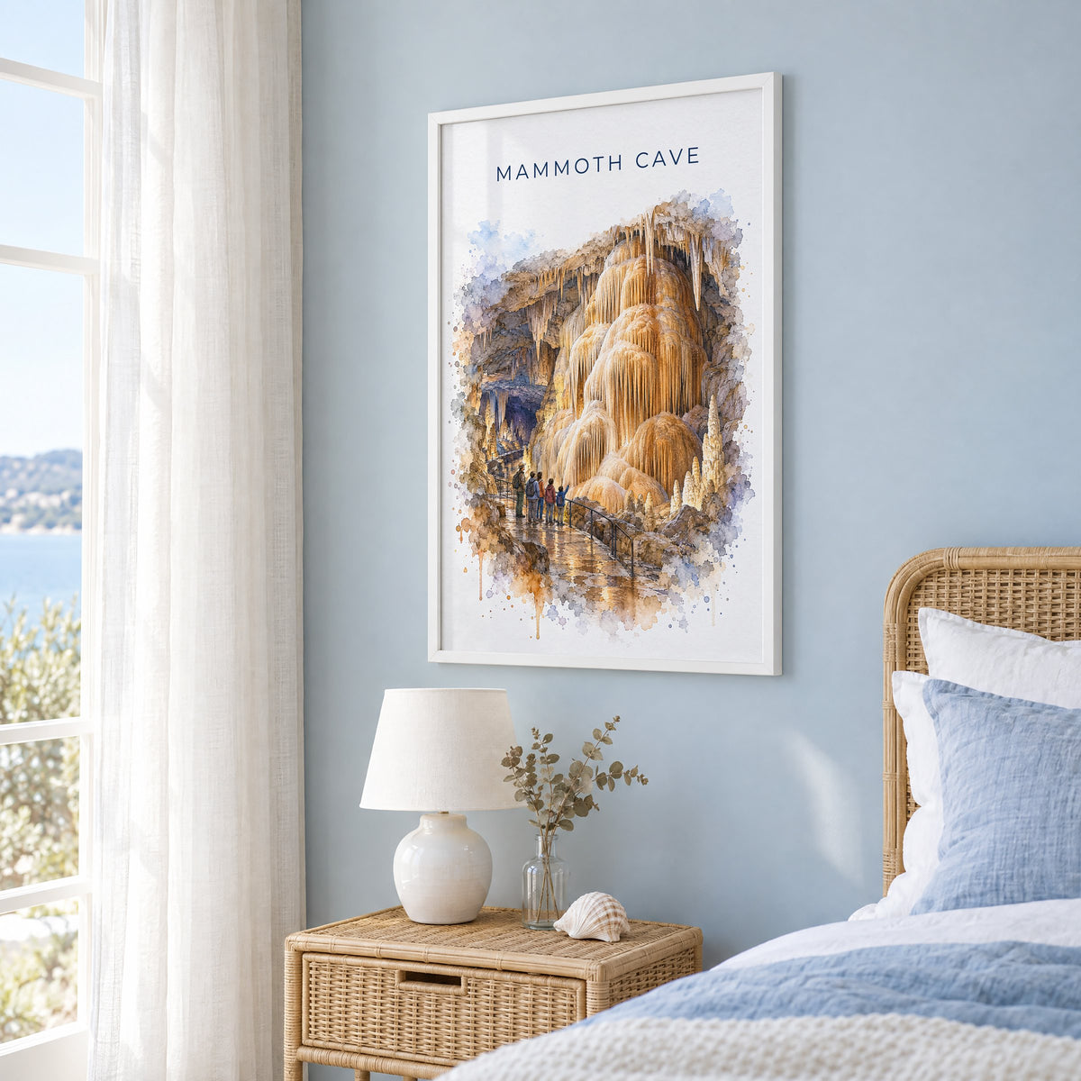 Mammoth Cave National Park watercolor print in a white frame on a pale blue wall beside a rattan bed in a coastal bedroom