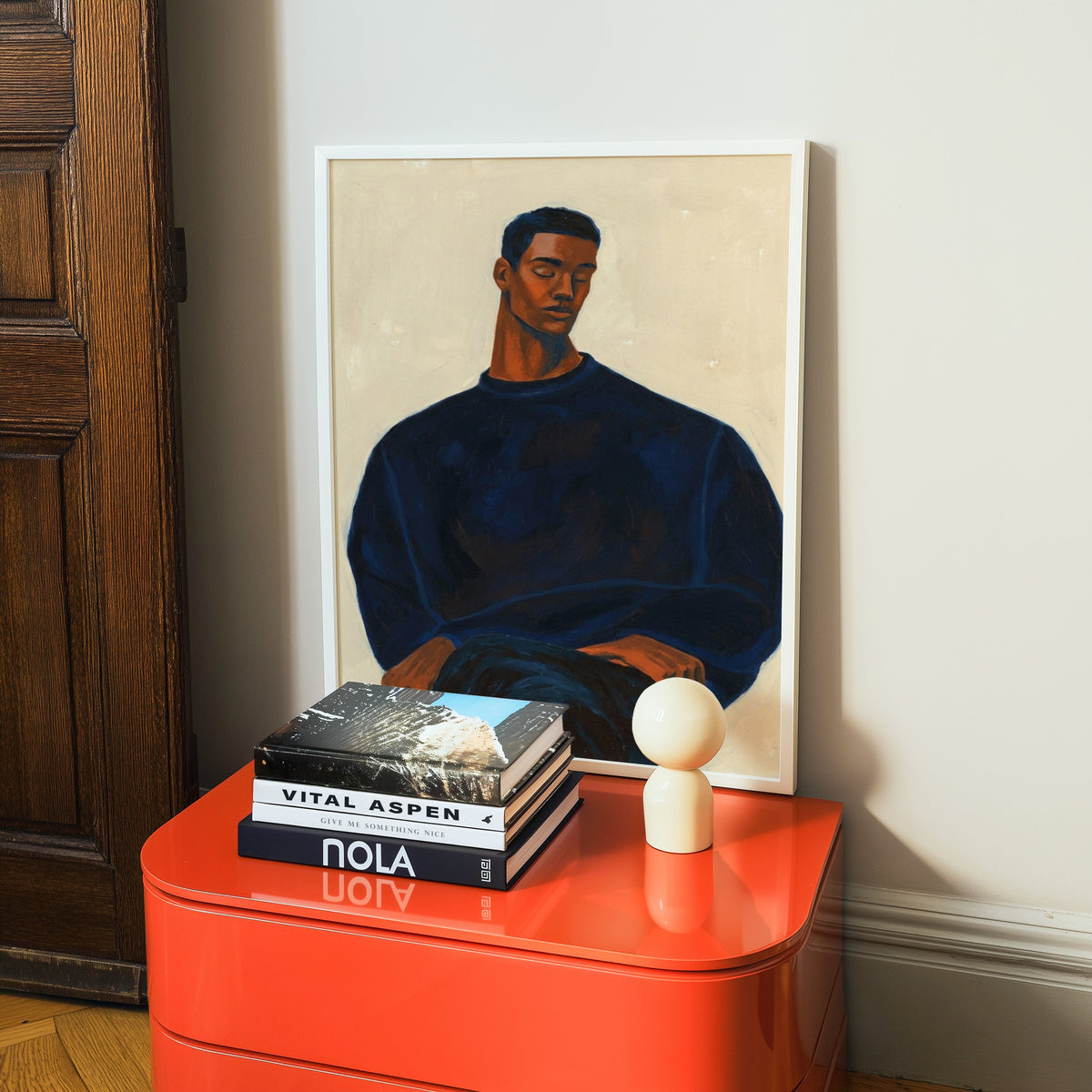 Modern male portrait print in a white frame on a glossy orange cabinet with books