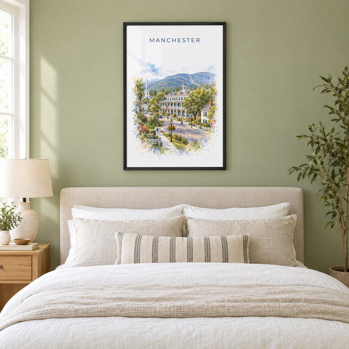 Manchester, Vermont watercolor print in a black frame above an upholstered headboard in a sage green bedroom