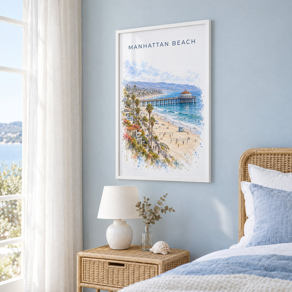 Manhattan Beach watercolor print in a white frame on a pale blue wall beside a rattan bed in a coastal bedroom