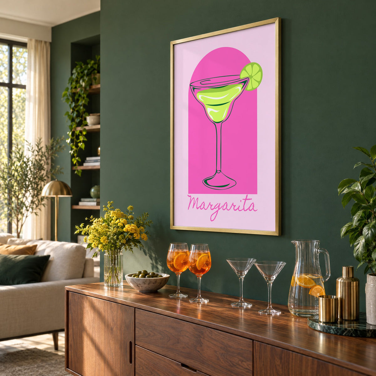 Margarita glass and lime pink arch print in a brass frame on a bottle green wall above a sideboard with spritz and martini glasses, seen at an angle