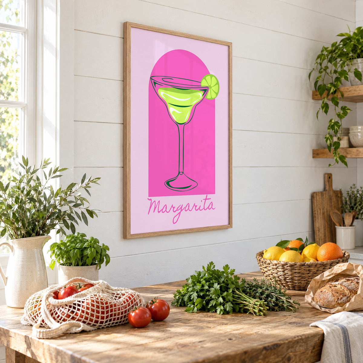 Margarita glass and lime pink arch print in an oak frame on a shiplap wall above a farm table with market tomatoes and citrus, seen at an angle