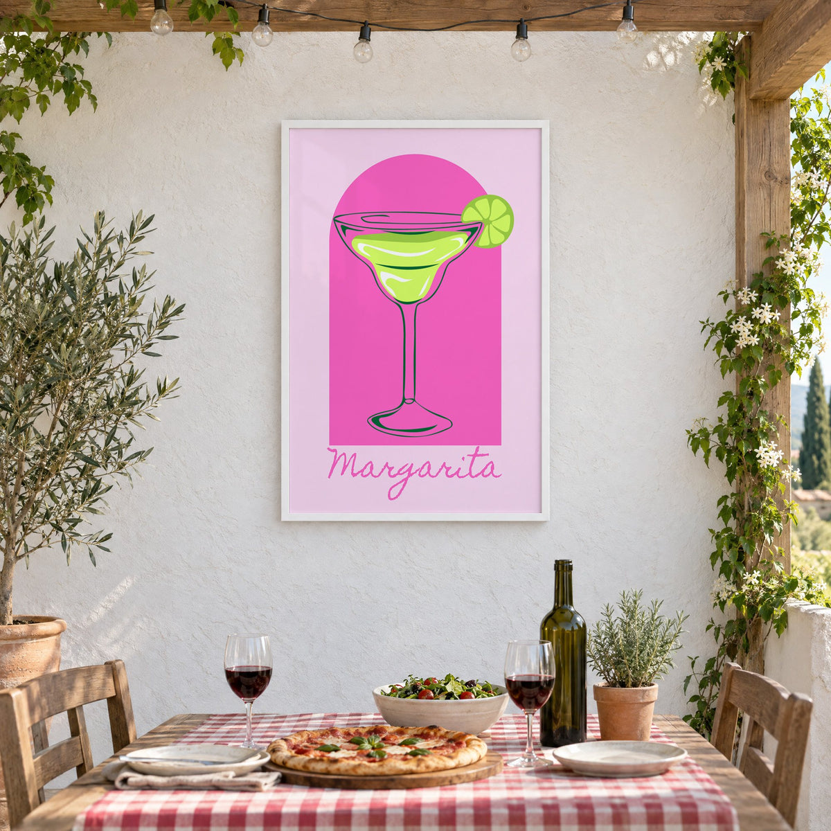 Margarita glass and lime pink arch print in a white frame on a stucco wall above a checked-cloth table with pizza and red wine