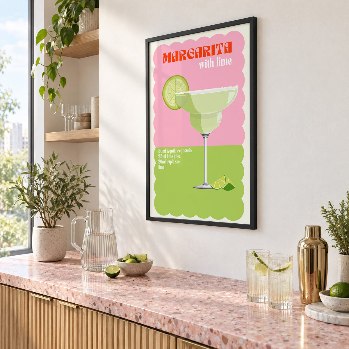 Margarita with lime scalloped print in a black frame above a pink terrazzo cocktail counter with limes, seen at an angle