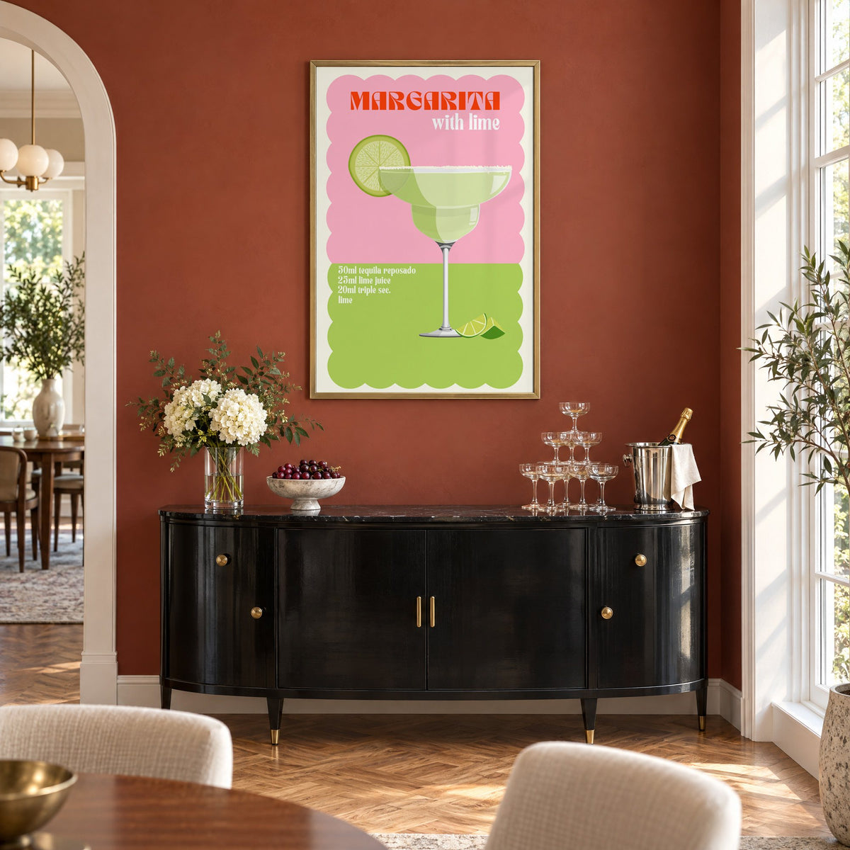 Margarita with lime scalloped print in a brass frame on a terracotta wall above a black buffet with a champagne tower